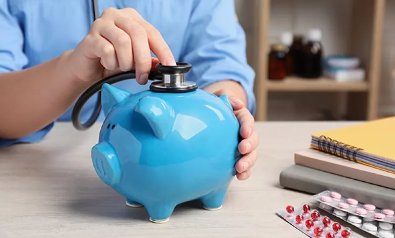 Nurse holding a stethoscope to a blue piggy bank